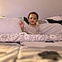 toddler, child, bed, bedding, pillow, blanket, smile, happy, indoors, cozy, sleepwear, person, young_child, curly_hair, waving, soft_lighting, home, comfort, cute, portrait