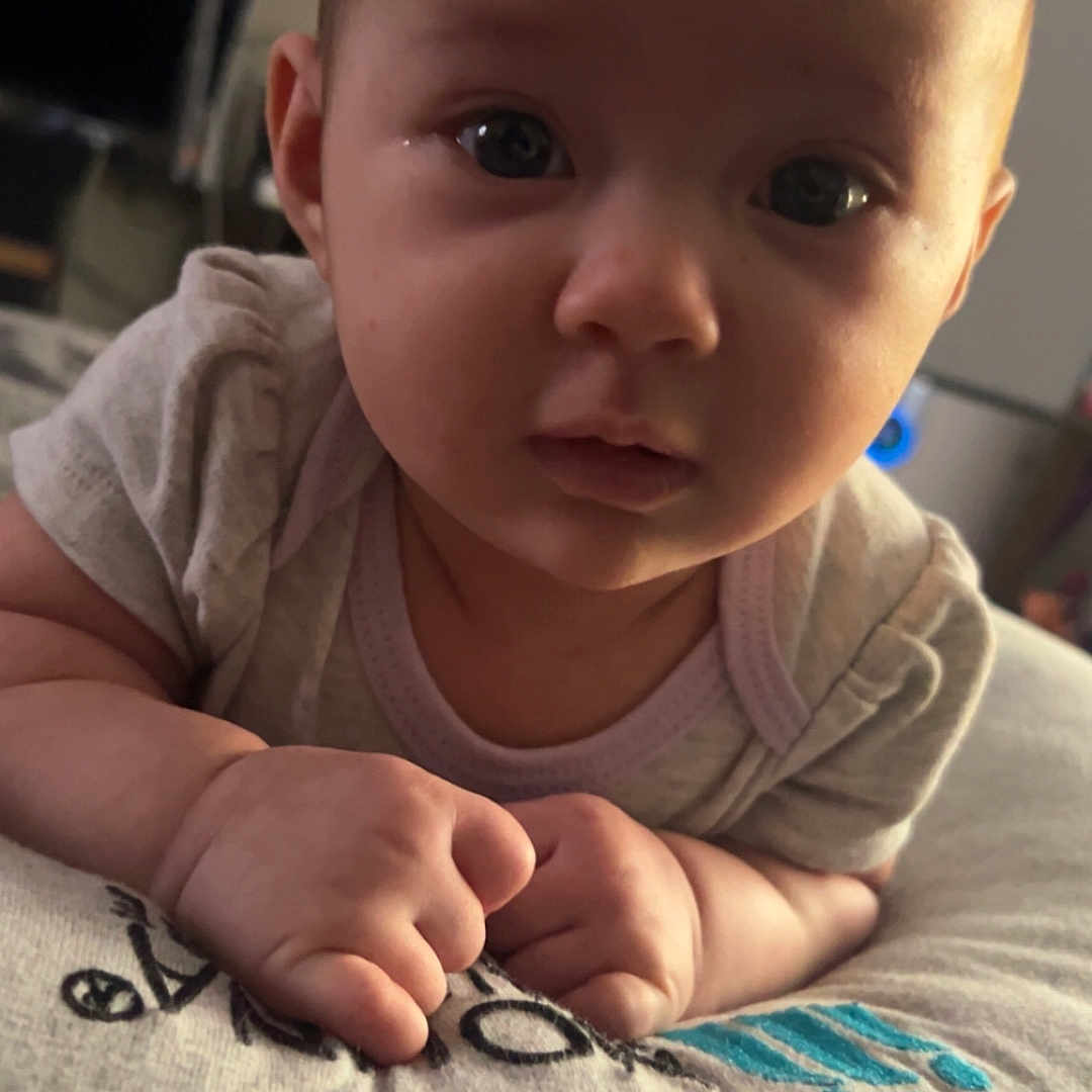 Lucille joined the competition — help win amazing prizes! baby, infant, child, face, portrait, hands, pillow, indoor, soft_lighting, curious, closeup, cute, young, person, skin, expression, resting, looking, cozy, casual