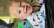 Asher is registered to the contest to win money with this photo: baby, child, plush_toy, stuffed_animal, sloth, alien, bed, blanket, space_poster, planet, room, indoor, smiling, happy, blue_eyes, light, window, clothing, toy, playful