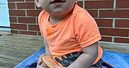 Asher joined the competition — help win amazing prizes! toddler, child, baby, blue_eyes, orange_shirt, brick_wall, wooden_floor, blanket, toy, socks, outdoor, curious, drool, sitting, casual_clothing, portrait, daylight, cute, person, young_child