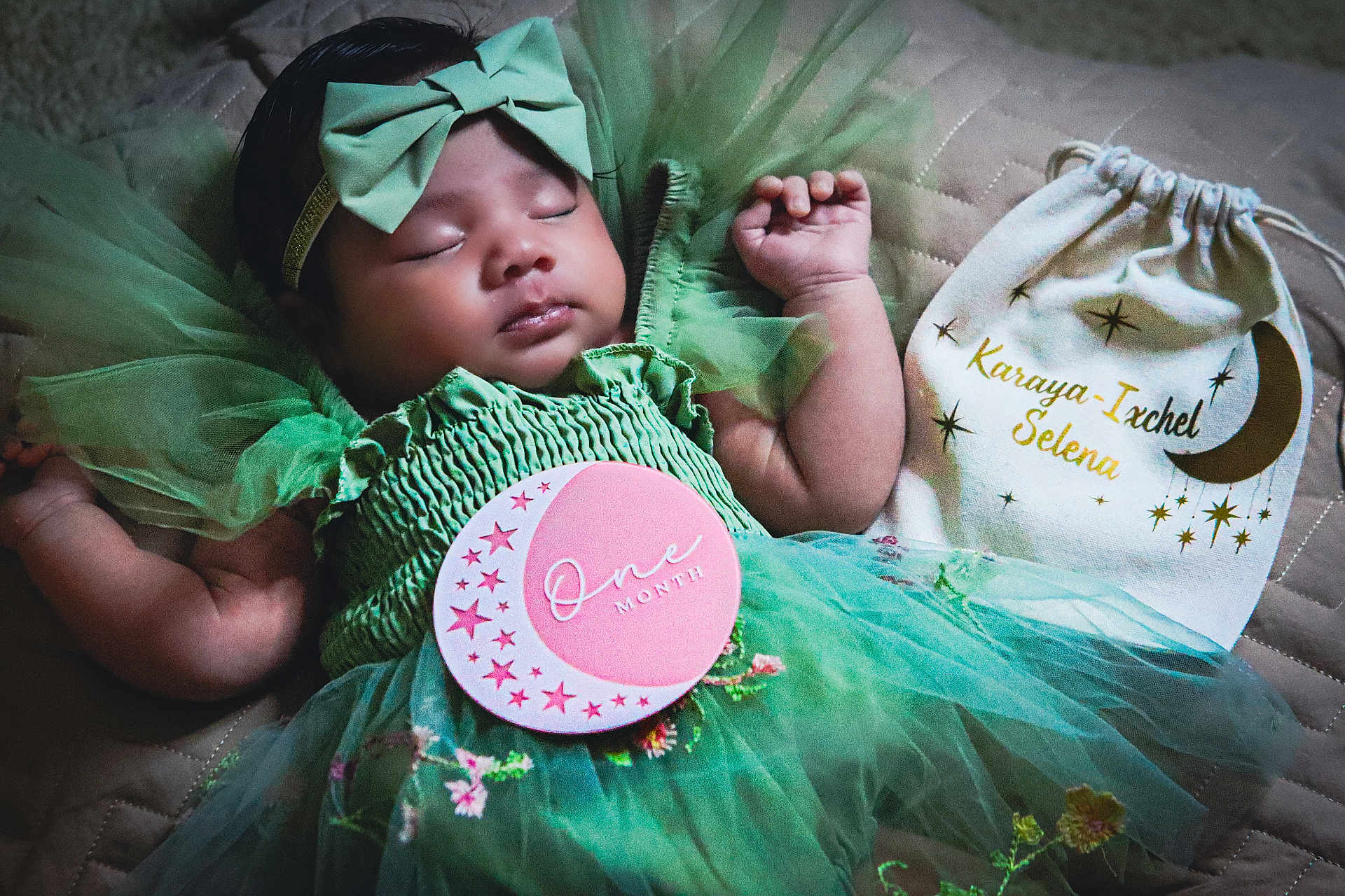Karaya is registered to the contest to win money with this photo: baby, sleeping, green_dress, headband, bow, milestone_card, one_month, quilted_blanket, decorative_bag, name_tag, infant, cute, portrait, tulle, soft_lighting, peaceful, hands_up, closeup, newborn, indoor