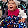 baby, child, infant, stroller, smiling, happy, outdoor, city, street, urban, portrait, hat, blanket, colorful, clothing, sweater, bib, seated, tree, building