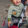 baby, child, toddler, smiling, happy, portrait, stroller, outdoor, night, street, sidewalk, urban, clothing, striped_sweater, gray_pants, colorful_socks, vehicle, parked_cars, pavement, candid