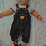 baby, infant, pacifier, denim_overalls, teddy_bear_patch, sneakers, blue_blanket, lying_down, cute, child, footwear, clothing, bracelet, indoors, person, young_child, soft_texture, head, small_arms, comfort