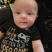 Eliana is registered to the contest to win money with this photo: baby, infant, child, person, face, eyes, shirt, text, hand, sitting, indoors, clothing, cute, portrait, young, human, expression, comfort, parent, humor