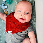 Ollie joined the competition — help win amazing prizes! baby, infant, smiling, red_bib, pacifier, toy_elephant, wooden_beads, grey_onesie, blue_eyes, chubby_cheeks, lying_down, changing_pad, patterned_text, close_up, portrait, skin, cute, nursery, accessory, arm