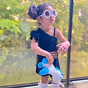 Angelina a rejoint le concours — aidez-le/la à gagner de superbes lots ! accessories, black_dress, blurred_background, child, cute, fashion, girl, hair_buns, indoors, leopard_print_belt, playful, portrait, pout, standing, stuffed_animal, sunglasses, toy, white_shoes, white_socks, window
