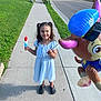 child, girl, popsicle, balloon, sidewalk, street, grass, summer, daylight, casual_clothing, smile, pigtails, footwear, outdoor, residential_area, balloon_character, happy, playful, neighborhood, concrete