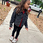 Kennedi is registered to the contest to win money with this photo: child, girl, sidewalk, black_denim_jacket, braided_hair, mickey_mouse_shoes, red_shirt, black_leggings, flowers, flower_pot, trees, parked_vehicle, white_truck, outdoor, suburban, concrete, casual_clothing, holding_object, daylight, curious