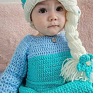 Mia joined the competition — help win amazing prizes! toddler, child, knitted_clothing, hat, braid, yarn, blue, turquoise, beads, earrings, sitting, portrait, indoor, soft_texture, pink_cushion, curly_hair_style, cute, young_child, face, eyes