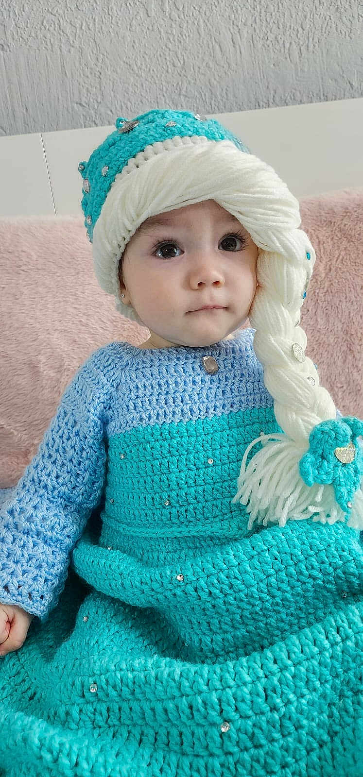Mia joined the competition — help win amazing prizes! toddler, child, knitted_clothing, hat, braid, yarn, blue, turquoise, beads, earrings, sitting, portrait, indoor, soft_texture, pink_cushion, curly_hair_style, cute, young_child, face, eyes