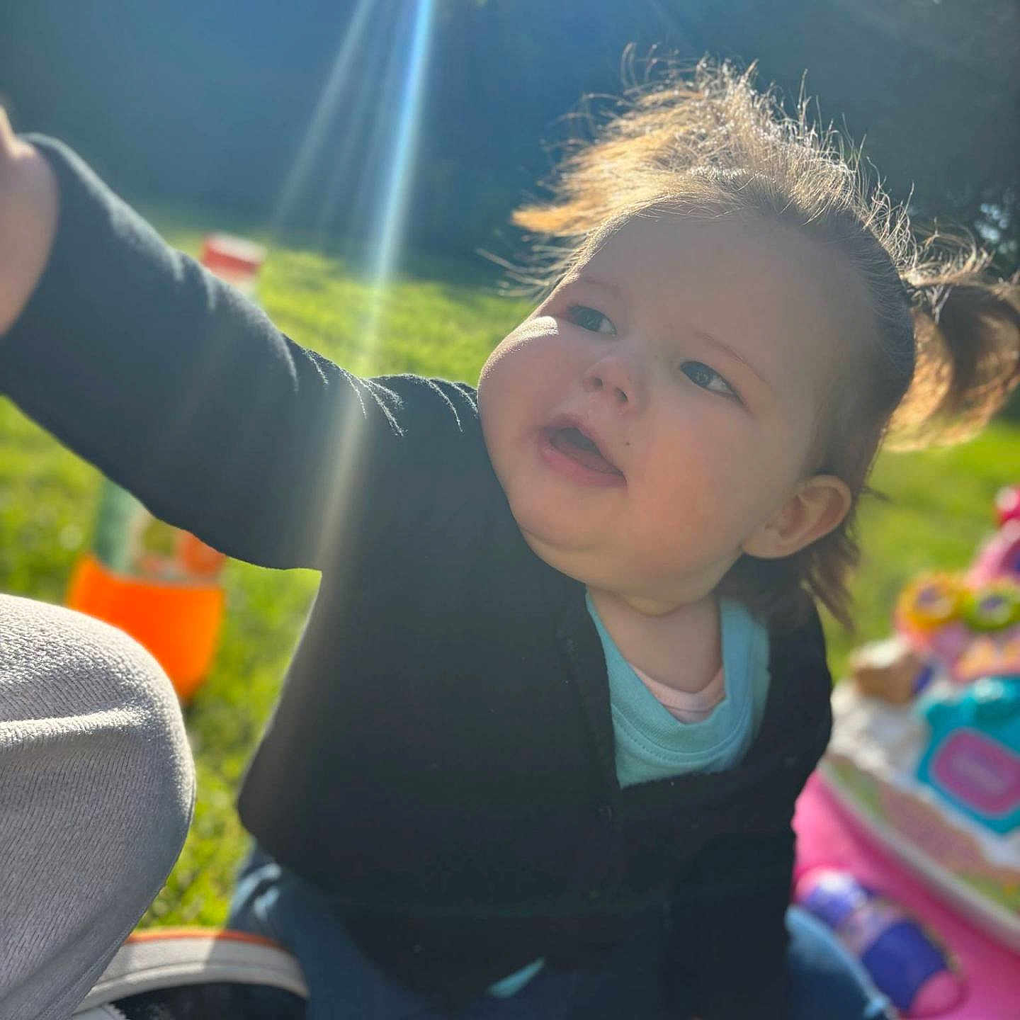 Lyana participe au concours pour gagner de l'argent avec cette photo : baby, black_jacket, blue_pants, child, cute, daylight, fun, grass, happy, nature, outdoor, person, pigtails, playtime, reaching_hand, smiling, summer, sunlight, toddler, toy