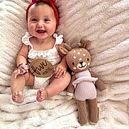 London joined the competition — help win amazing prizes! baby, infant, smiling, red_headband, white_outfit, wooden_sign, five_months, knitted_toy, deer_doll, plush_blanket, cute, happy, sitting, portrait, indoors, child, soft_texture, cozy, accessory, bracelet