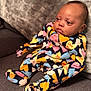 baby, infant, pajamas, colorful_clothing, heart_pattern, couch, blanket, furniture, indoors, child, person, cute, soft_texture, relaxed, seated, portrait, young, warm, comfort, home