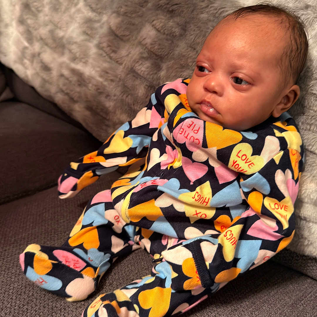 Gianna Jean Spivey is registered to the contest to win money with this photo: baby, blanket, child, colorful_clothing, comfort, couch, cute, furniture, heart_pattern, home, indoors, infant, pajamas, person, portrait, relaxed, seated, soft_texture, warm, young