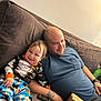 Isaiah Mendez joined the competition — help win amazing prizes! toddler, adult, couch, smile, pajamas, remote_control, cardboard_box, tattoo, blue_shirt, relaxed, indoor, family, child, person, seated, brown_couch, happy, casual, living_room, home