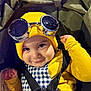 baby, child, goggles, yellow_hat, beanie, checkered_clothing, stroller, harness, smiling, face, cute, infant, portrait, childwear, black_straps, closeup, indoor, happy, person, babywearing