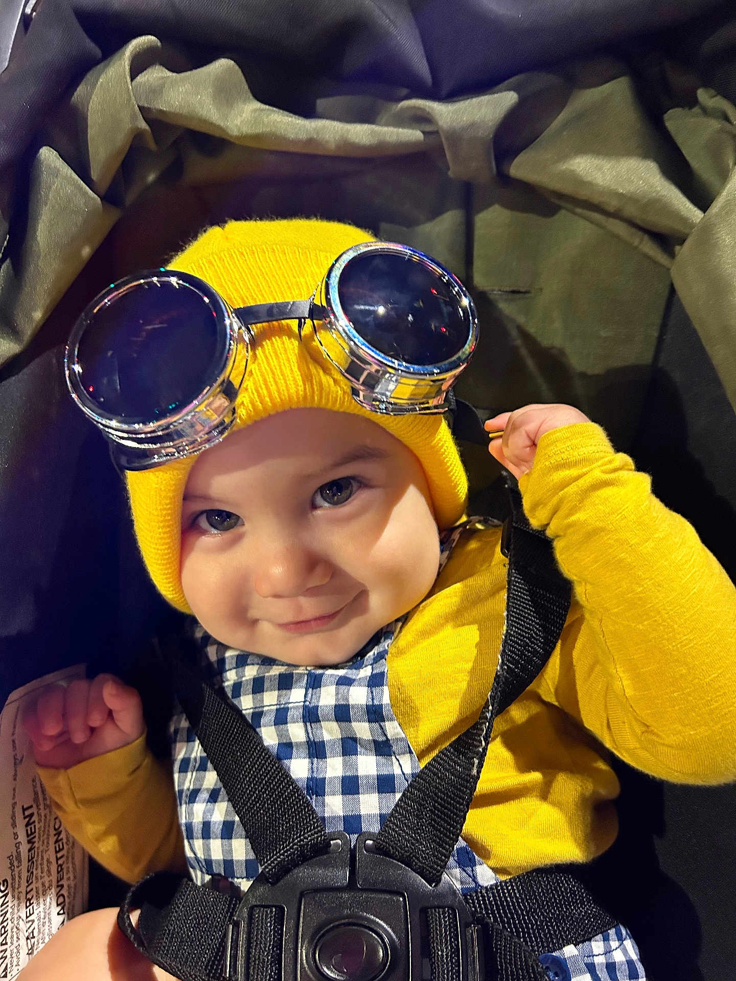 Isaiah Mendez joined the competition — help win amazing prizes! baby, child, goggles, yellow_hat, beanie, checkered_clothing, stroller, harness, smiling, face, cute, infant, portrait, childwear, black_straps, closeup, indoor, happy, person, babywearing