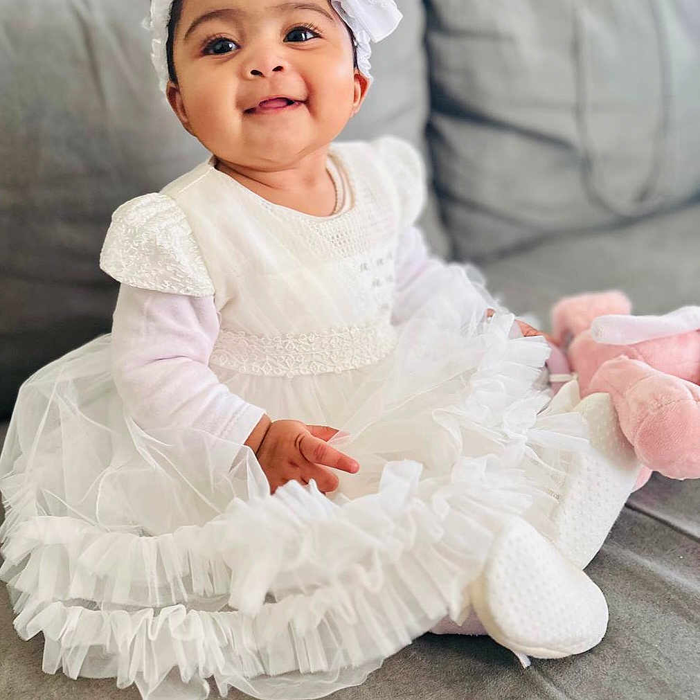 Lyana participe au concours pour gagner de l'argent avec cette photo : accessories, baby, babylaughing, bonnet, cap, clothing, costume, couch, dress, face, furniture, happy, hat, head, person, photography, portrait, sitting, sleeve, smile