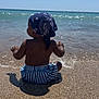 toddler, child, beach, water, sea, sand, sunny, bandana, shorts, striped, back_view, summer, outdoor, vacation, sunlight, waves, nature, shore, sitting, play