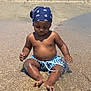 toddler, child, beach, sand, water, swim_shorts, bandana, sunny, summer, umbrella, shoreline, vacation, play, barefoot, outdoor, cute, relaxation, holiday, sea, sunlight