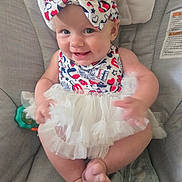 Juni is registered to the contest to win money with this photo: baby, child, smiling, bow, headband, dress, tulle_skirt, sitting, chair, cushion, cute, happy, indoor, person, infant, skin, foot, hand, face, dimples