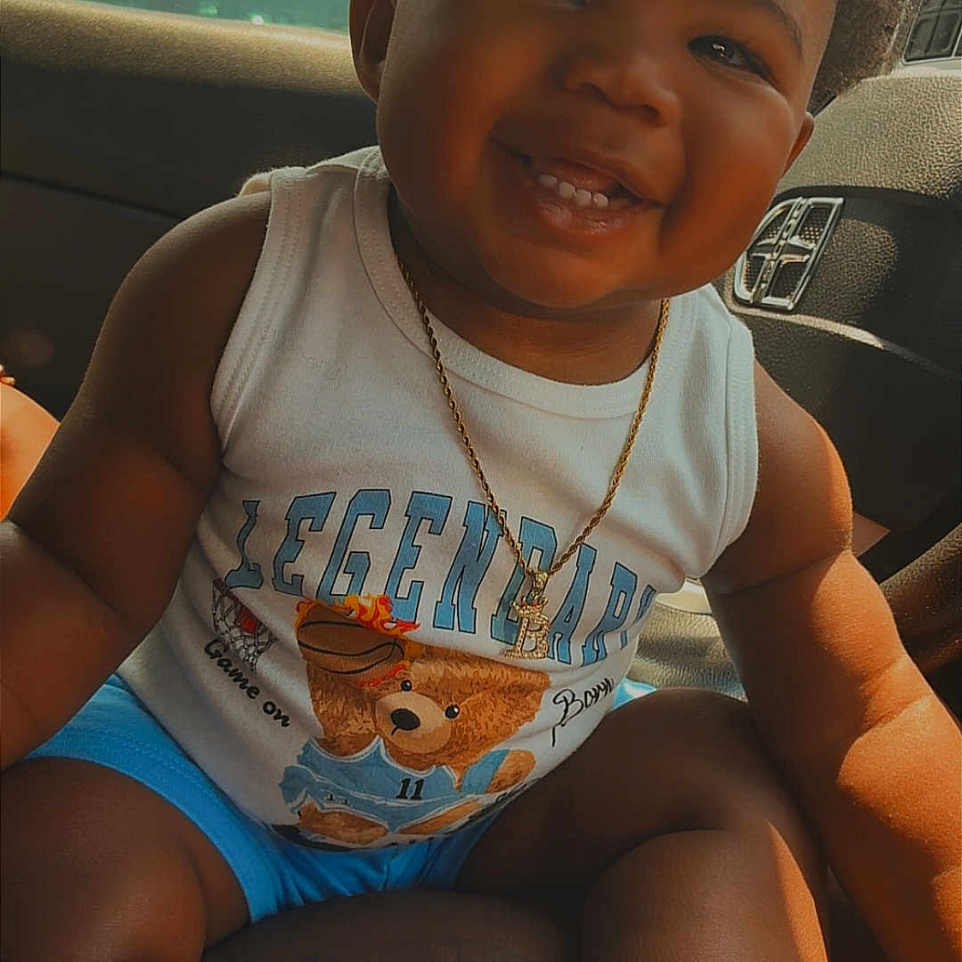 Bralyn joined the competition — help win amazing prizes! toddler, smiling, child, sitting, car_interior, tank_top, shorts, sneakers, socks, gold_chain, cute, happy, portrait, baby, indoors, seat, clothing, footwear, person, sunlight