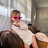 toddler, child, sunglasses, pink, snack, couch, leather, living_room, curtains, window, casual_clothing, indoor, person, furniture, relaxed, cute, home, smile, hair, seat