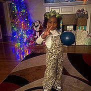 Demei joined the competition — help win amazing prizes! child, girl, leopard_print, overalls, green_bow, peace_sign, blue_ball, rug, living_room, christmas_tree, christmas_lights, gifts, holiday_decor, wooden_floor, fireplace, santa_figure, smiling, indoor, festive, happy
