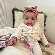 Bella participe au concours pour gagner de l'argent avec cette photo : baby, child, smiling, headband, pink_bow, couch, blanket, pillow, indoor, cute, infant, clothing, portrait, cozy, sitting, hand, texture, soft, warm, happy