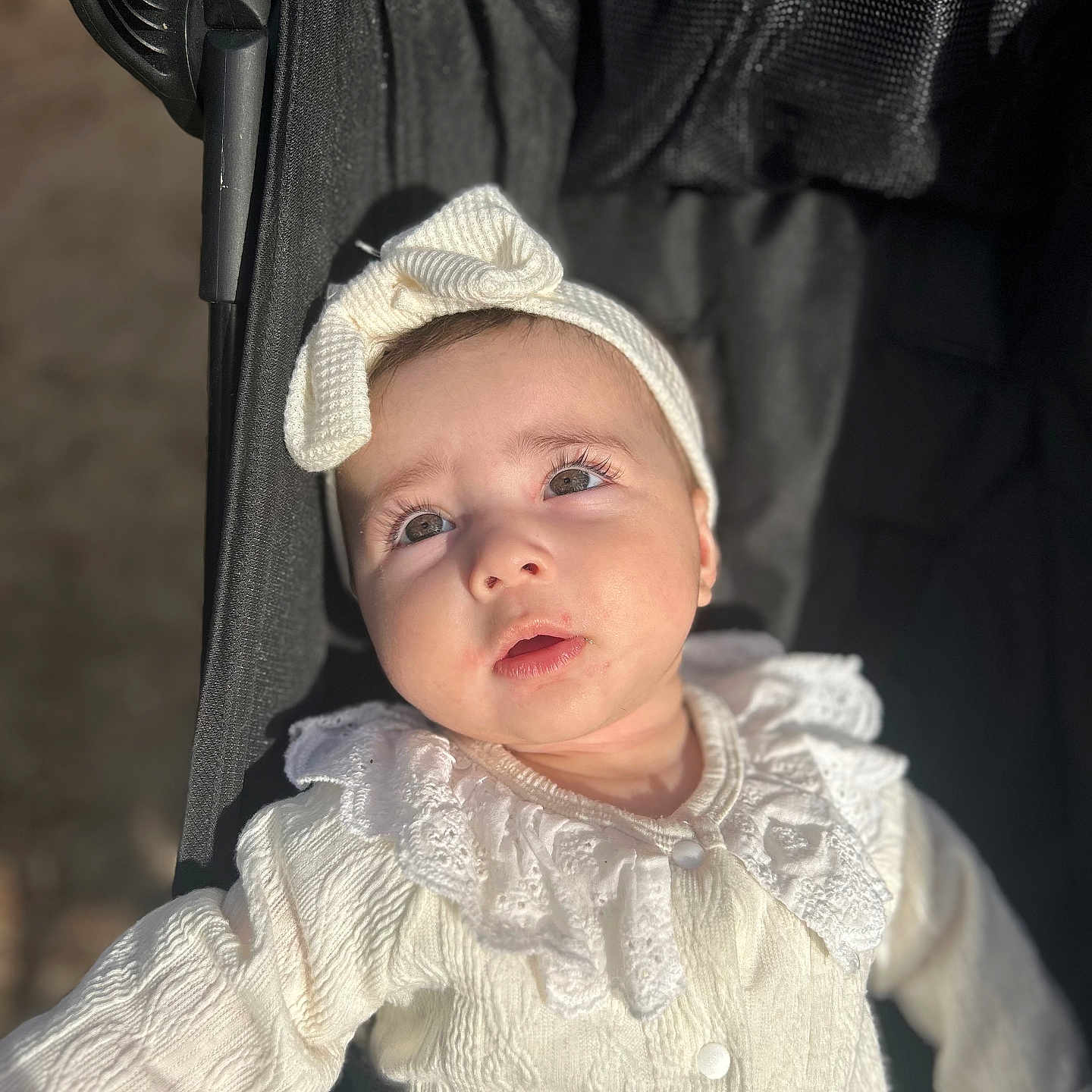 Bella participe au concours pour gagner de l'argent avec cette photo : baby, infant, stroller, white_clothing, headband, bow, sunlight, portrait, closeup, child, cute, outdoor, texture, fabric, face, expression, seatbelt, black_stroller, soft_light, person