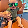 Jameson is registered to the contest to win money with this photo: baby, child, sunglasses, green, chair, hand, pacifier, plush_toy, indoor, window, reflection, smiling, happy, cute, legs, feet, person, casual_clothing, short_sleeves, modern
