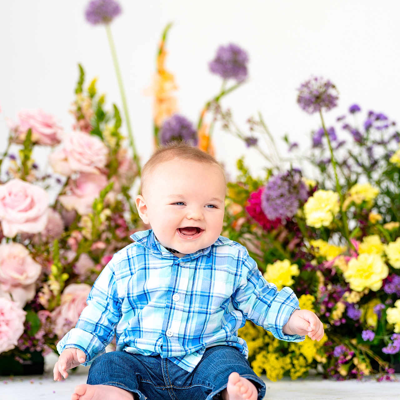 Jameson is registered to the contest to win money with this photo: baby, background, barefoot, blue_shirt, bright, child, colorful, cute, floral, flowers, happy, indoors, infant, jeans, nature, plaid, portrait, sitting, smiling, studio