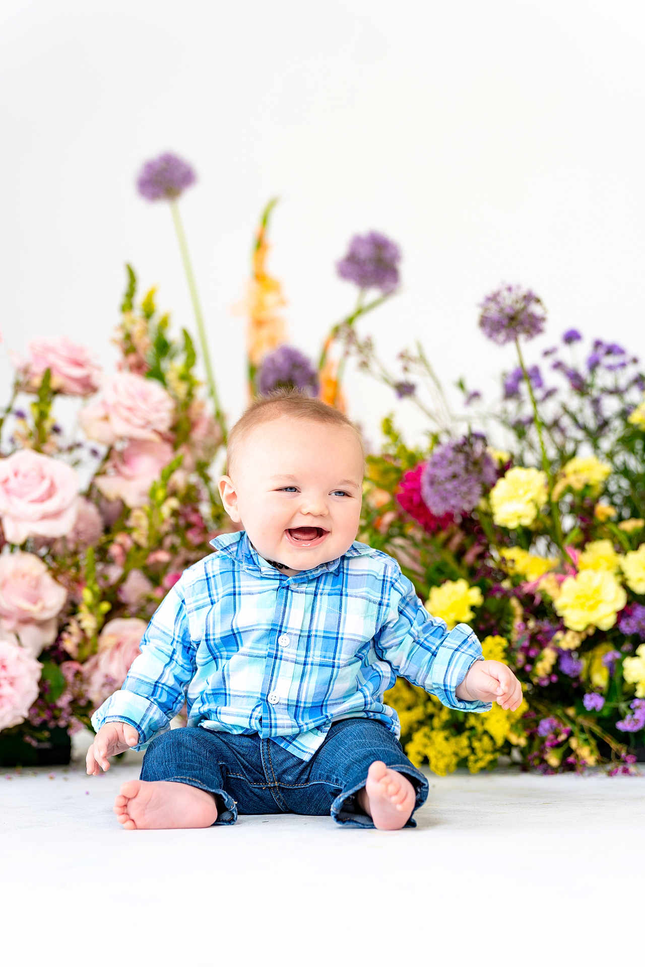 Jameson is registered to the contest to win money with this photo: baby, child, smiling, sitting, barefoot, blue_shirt, jeans, flowers, colorful, background, happy, indoors, plaid, cute, portrait, infant, floral, nature, bright, studio