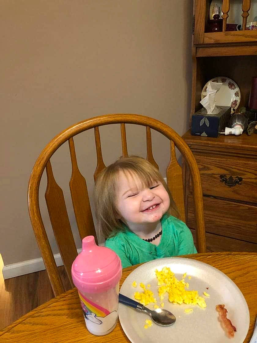 Hadleigh is registered to the contest to win money with this photo: baby_food, baby_playing_with_toys, bookcase, chair, child, comfort_food, dishware, fun, household_supply, joy, person, picture_frame, plastic_bottle, plate, room, shelf, shelving, smile, spoon, table