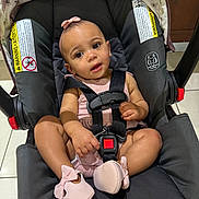 Laylani is registered to the contest to win money with this photo: baby, car_seat, infant, pink, bow, shoes, straps, sitting, cute, child, indoor, floor, warning_label, headband, clothing, black, seat, person, young_child, expression