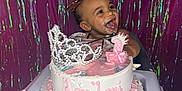Laylani is registered to the contest to win money with this photo: baby, birthday, cake, frosting, highchair, tiara, number_one_candle, pink, celebration, smiling, happy, party, ribbons, decorations, face, child, festive, portrait, young, fun