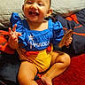 Azalea is registered to the contest to win money with this photo: baby, child, smiling, sitting, blue_clothing, yellow_clothing, indoor, carpet, toy, happy, person, face, cushion, red_carpet, wooden_toy, home, casual, cute, infant, portrait