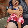 toddler, child, smiling, hat, dress, stars, stripes, adult, lap, outside, brick_wall, concrete, person, happy, casual_clothing, summer, barefoot, family, candid, portrait