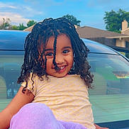 Hierani joined the competition — help win amazing prizes! child, smiling, curly_hair, braids, yellow_shirt, purple_pants, car, hood, outdoor, daylight, suburban, house, sky, happy, playful, portrait, clothing, person, nature, casual