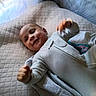 baby, infant, smile, face, onesie, blanket, cushion, bed, happy, child, portrait, indoor, young, cute, fist, clothing, person, lying_down, head, skin