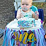 baby, birthday, cake, high_chair, sprinkles, messy, outdoor, celebration, toddler, food, hands, face, blue, purple, white, decorations, party, child, seat, first_birthday