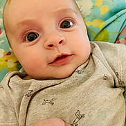 Bonnie is registered to the contest to win money with this photo: baby, infant, close_up, face, eyes, onesie, grey_clothing, hand, curious_expression, lying_down, blanket, floral_pattern, cute, child, portrait, skin, young, indoors, person, soft_light