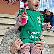 Victoria participe au concours pour gagner de l'argent avec cette photo : toddler, child, person, pom_pom, green_shirt, pink_pants, sneakers, knitted_sweater, bleachers, outdoor, woman, sunglasses, metal_roof, fence, excitement, smile, hands, sports_event, stadium, casual_clothing