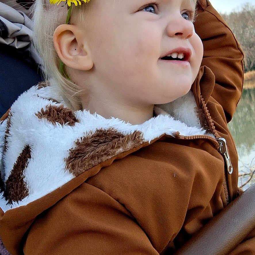 Victoria a rejoint le concours — aidez-le/la à gagner de superbes lots ! toddler, child, outdoor, sky, flower, yellow_flower, ponytail, brown_jacket, smile, face, profile, cute, nature, daylight, person, young_child, portrait, happy, warm_clothing, scenic