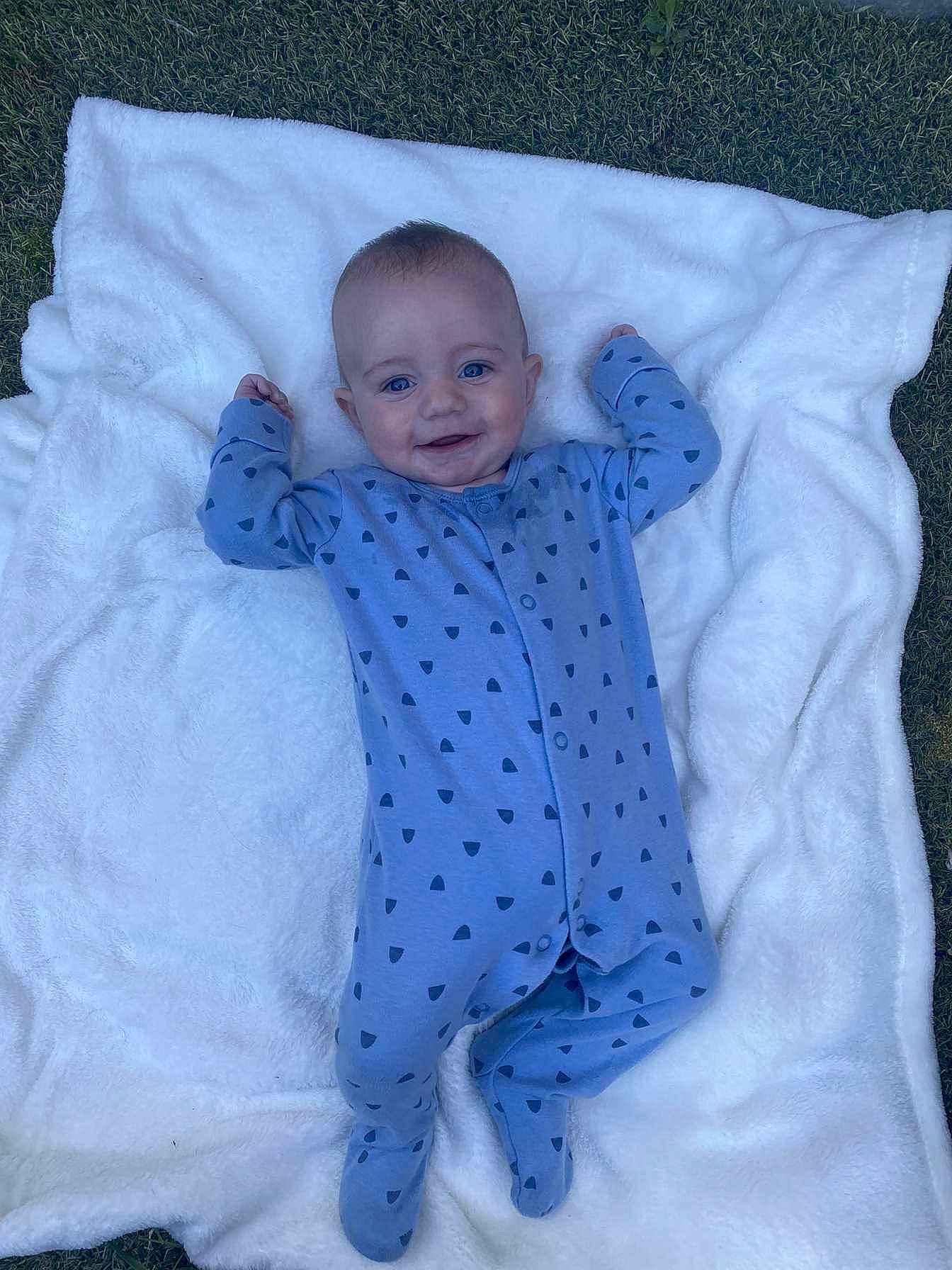 Arlo joined the competition — help win amazing prizes! baby, blue_onesie, blanket, grass, smiling, infant, outdoors, footed_pajamas, happy, cute, child, lying_down, patterned_clothing, soft_blanket, nature, young_child, face, portrait, one_person, daylight