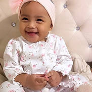 Ayla is registered to the contest to win money with this photo: baby, child, smiling, headband, bow, floral, onesie, couch, plush, tufted, hairbrush, infant, cute, happy, indoors, portrait, sitting, clothing, face, person