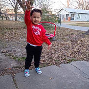 Kasai is registered to the contest to win money with this photo: child, toddler, curly_hair, red_sweatshirt, sneakers, raised_hand, smile, backyard, playground_equipment, house, sidewalk, pavement, leaf_litter, bare_trees, grass, fence, casual_clothing, portrait, daytime, person