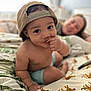 toddler, child, baby, cap, bed, sheet, cheetah_print, hand, face, smile, adult, blurred_background, indoor, person, curious, skin, furniture, casual, resting, home