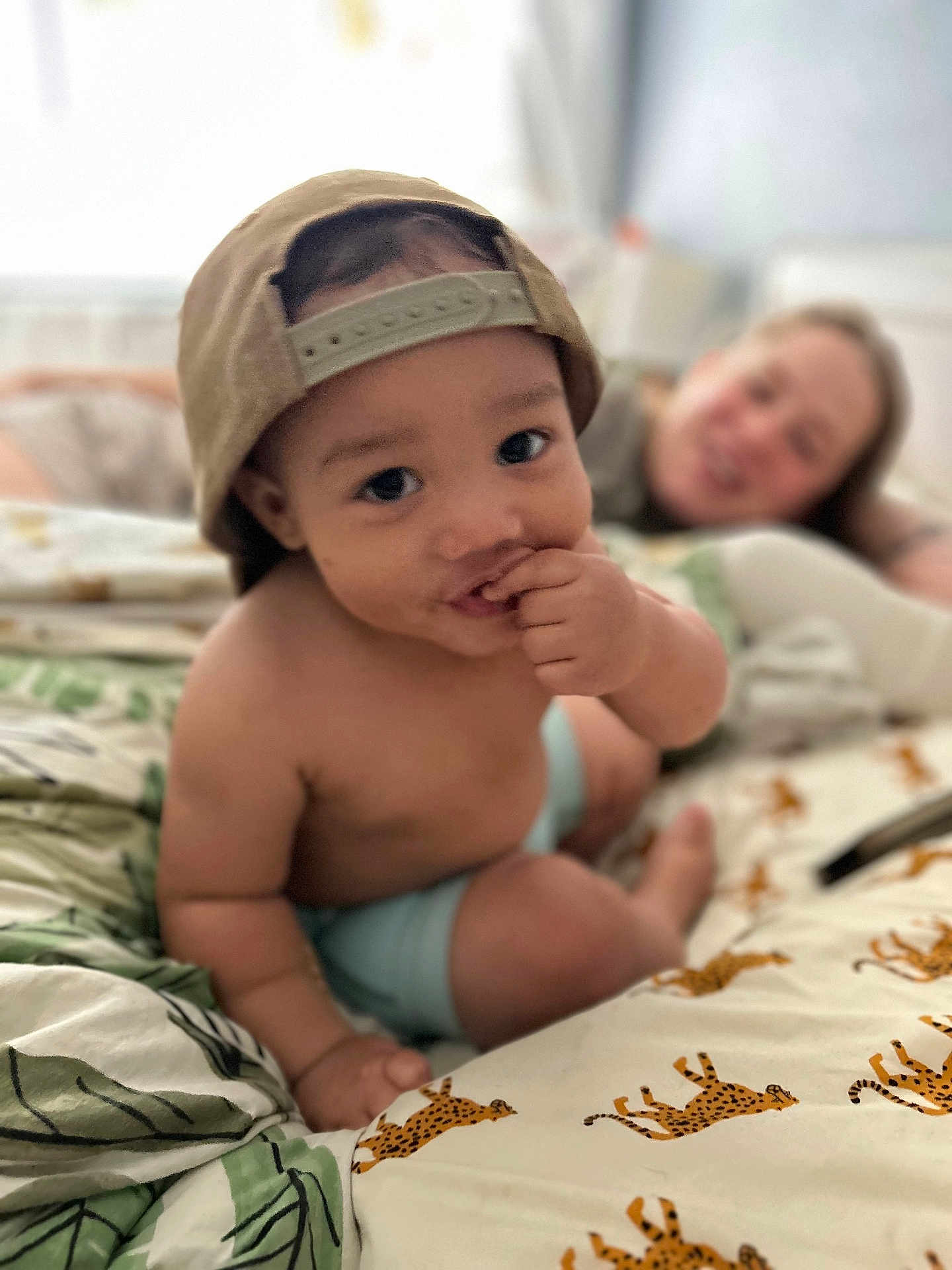 Jackson joined the competition — help win amazing prizes! toddler, child, baby, cap, bed, sheet, cheetah_print, hand, face, smile, adult, blurred_background, indoor, person, curious, skin, furniture, casual, resting, home